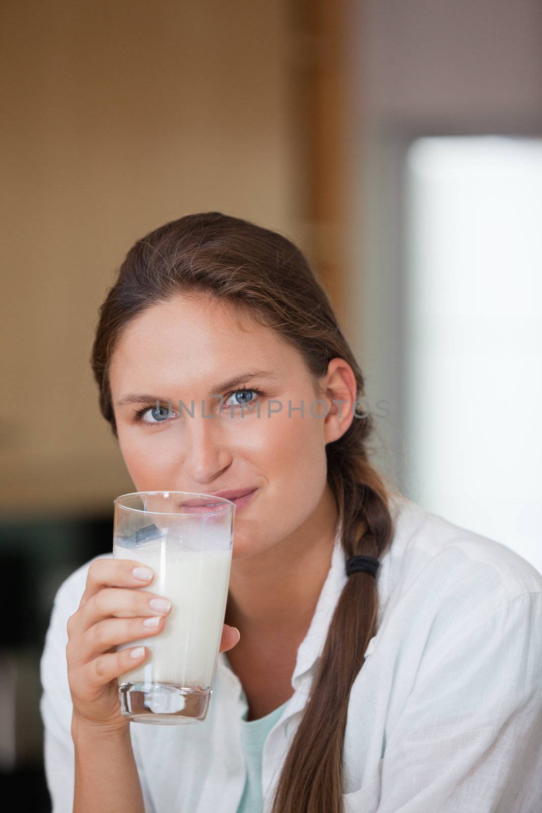 Woman drinking a glass of milk while looking the camera in a kitchen