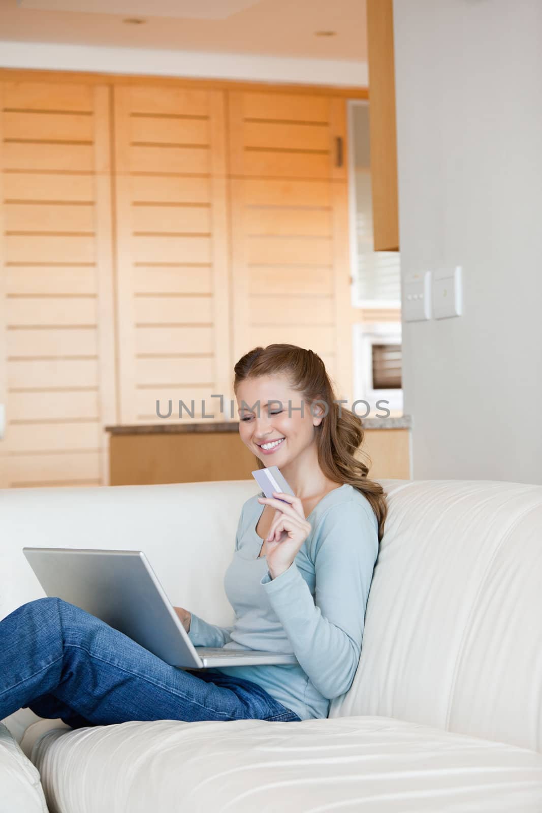 Woman using a laptop while holding a card in a sitting room