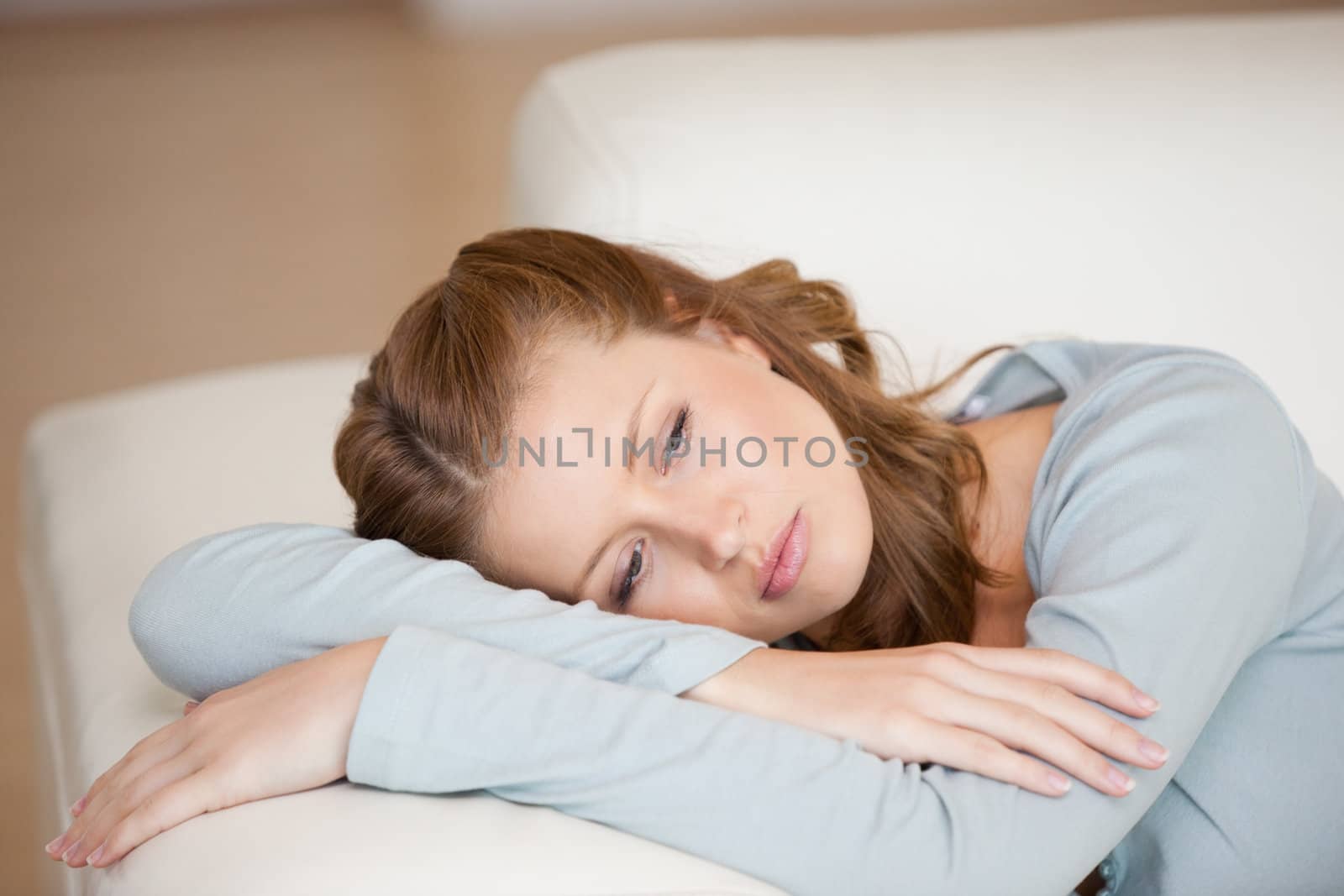 Woman lying on a sofa crossing her arms looking down indoors
