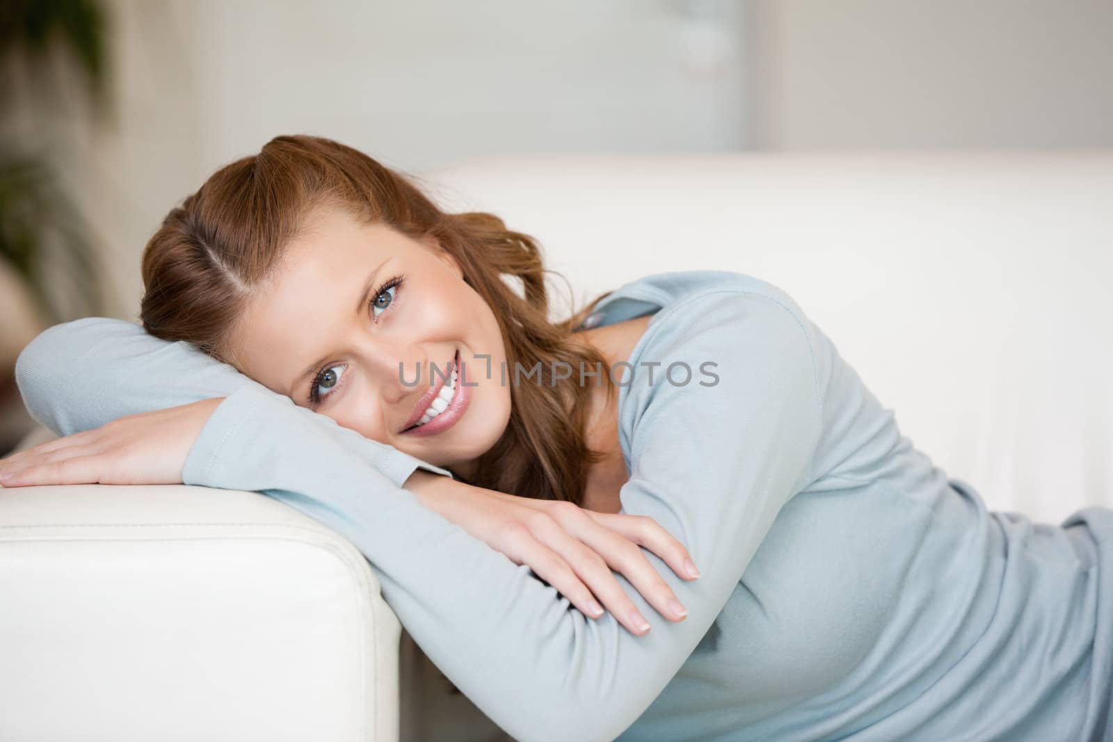 Smiling Woman crossing her arms while lying on a sofa indoor