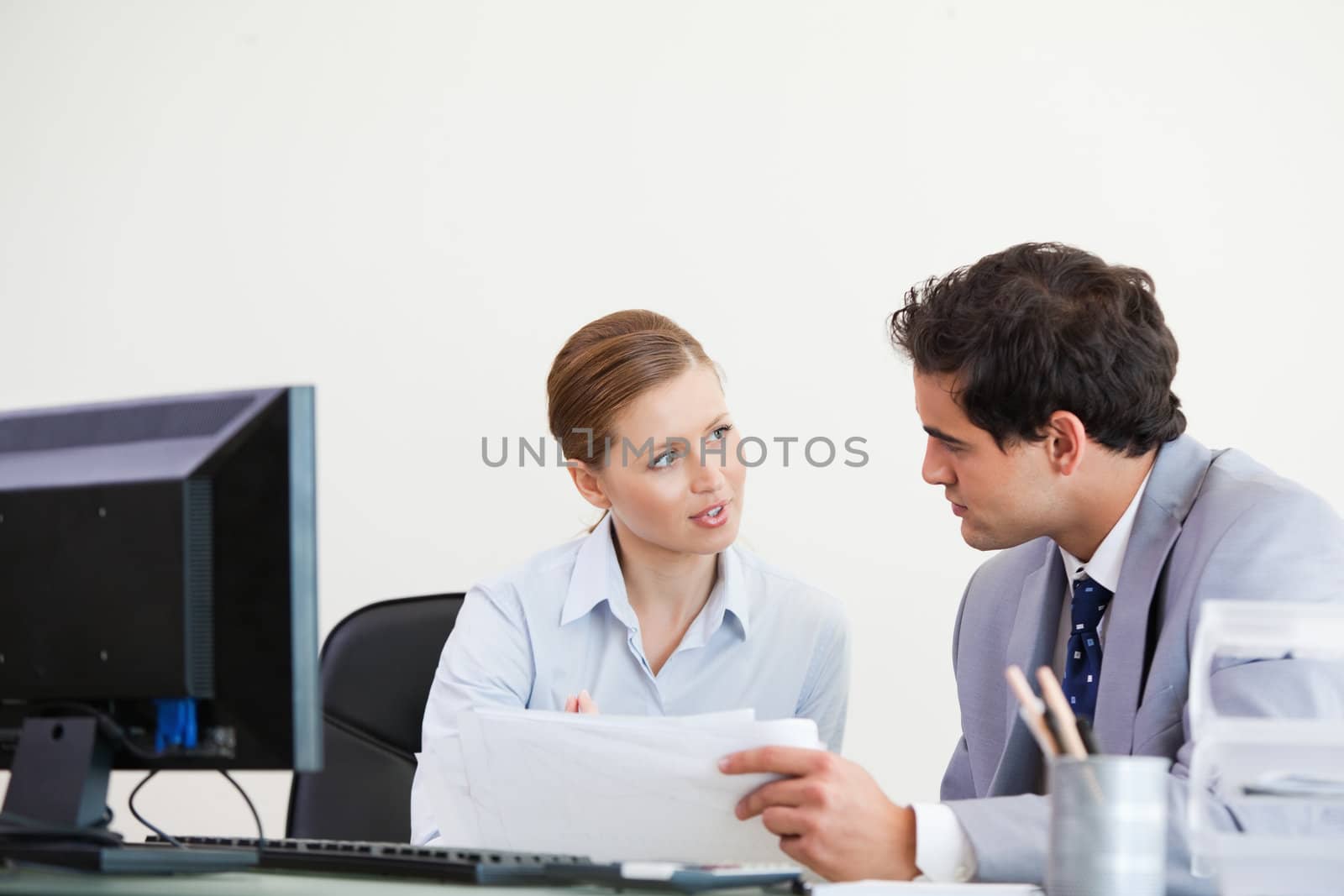 Colleagues talking while holding a sheet against grey background