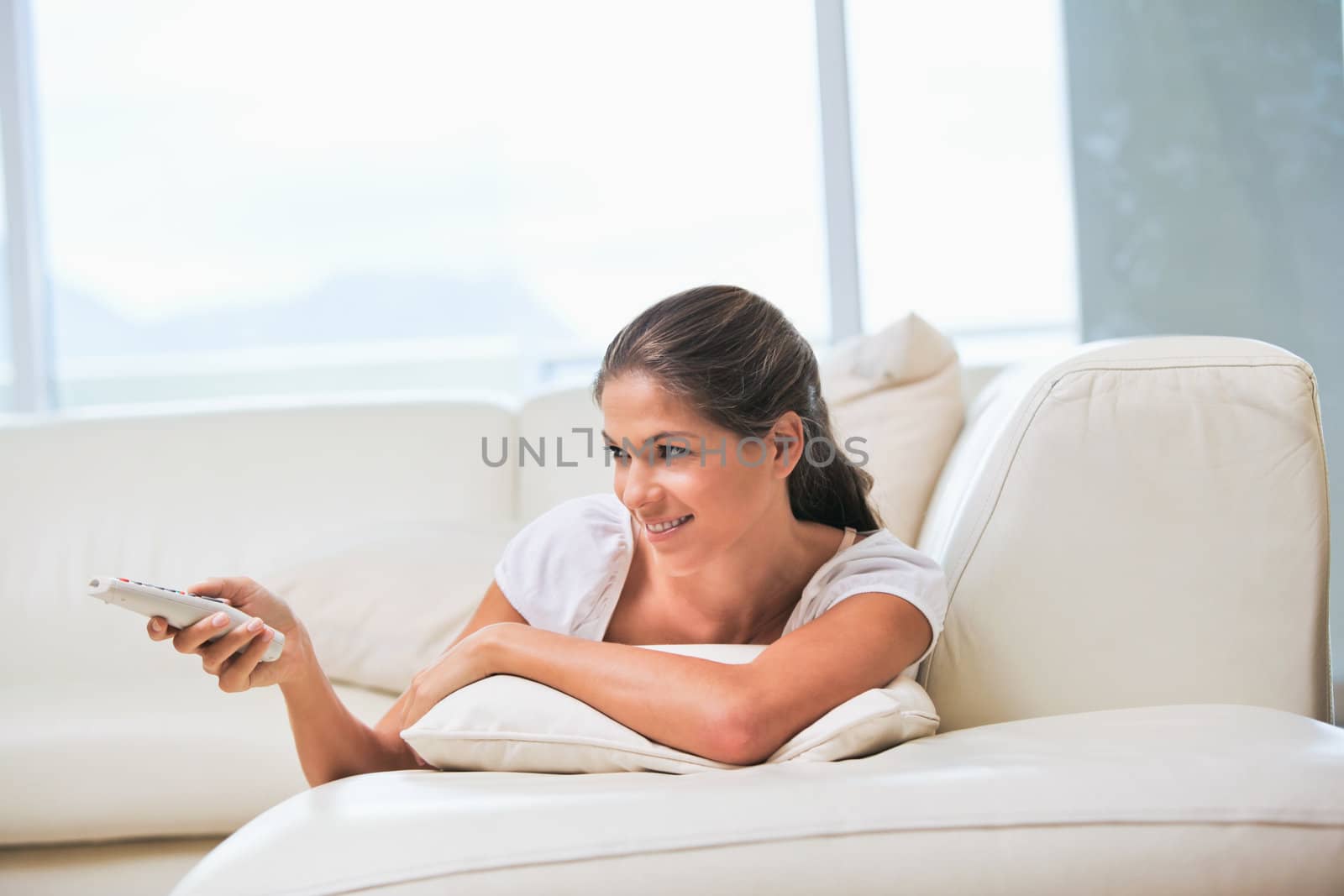 Woman lying on a sofa while holding a remote by Wavebreakmedia