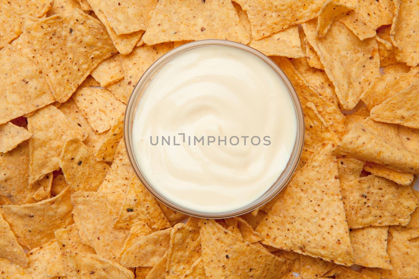 Bowl of dip placed among nachos against a white background