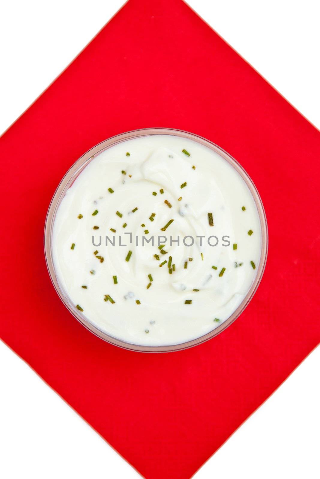 Close up of a bowl of white dip with herbs on a red napkin against a white background