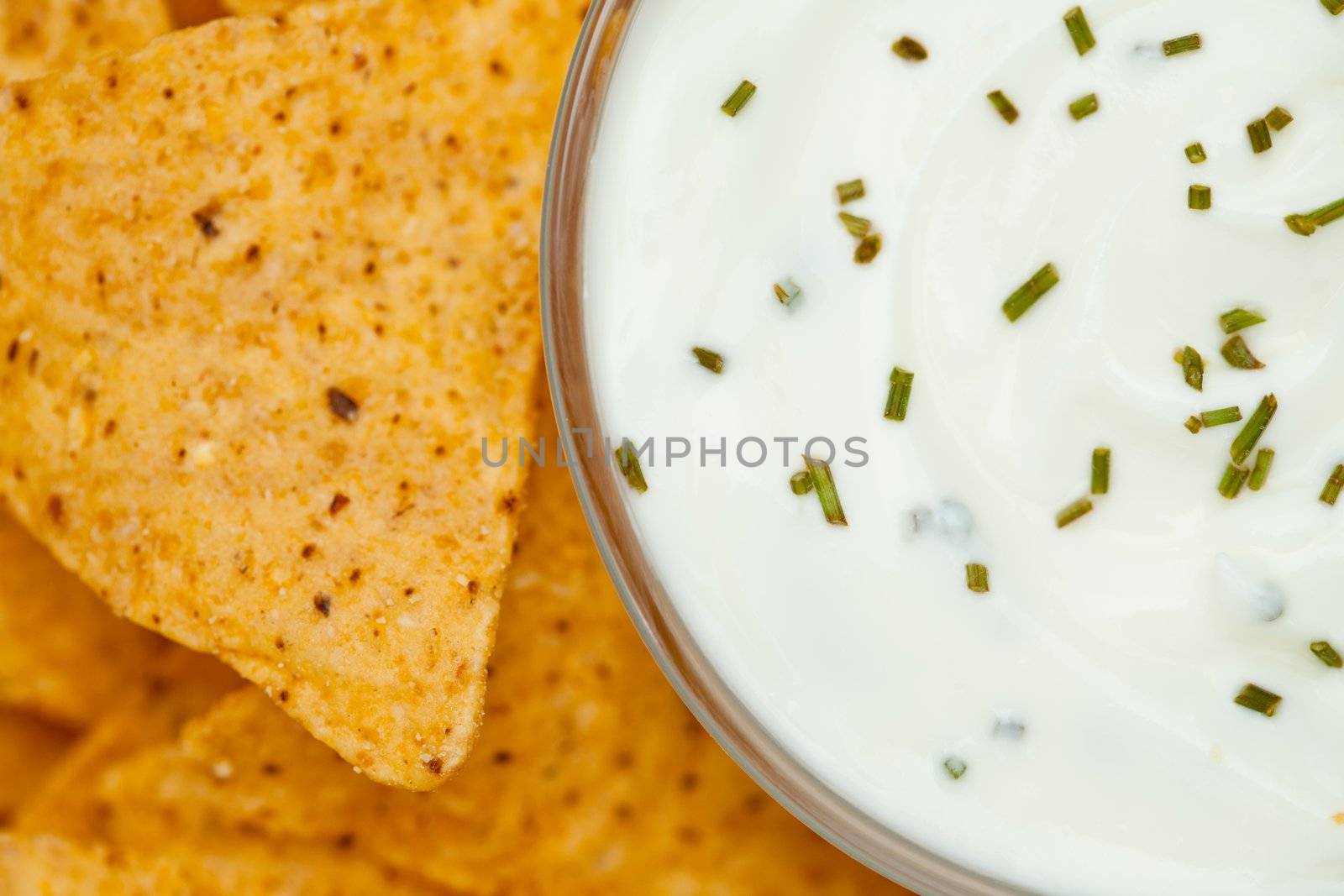 Close up of a bowl of white dip with herbs  beside nachos