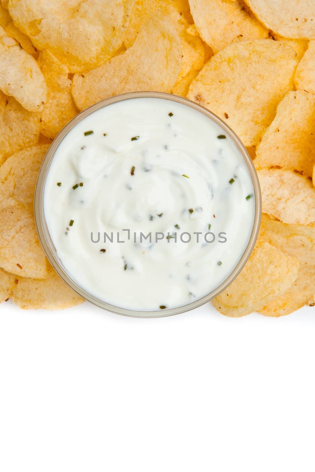 Close up of a bowl of white dip with herbs surrounded by nachos against a white background