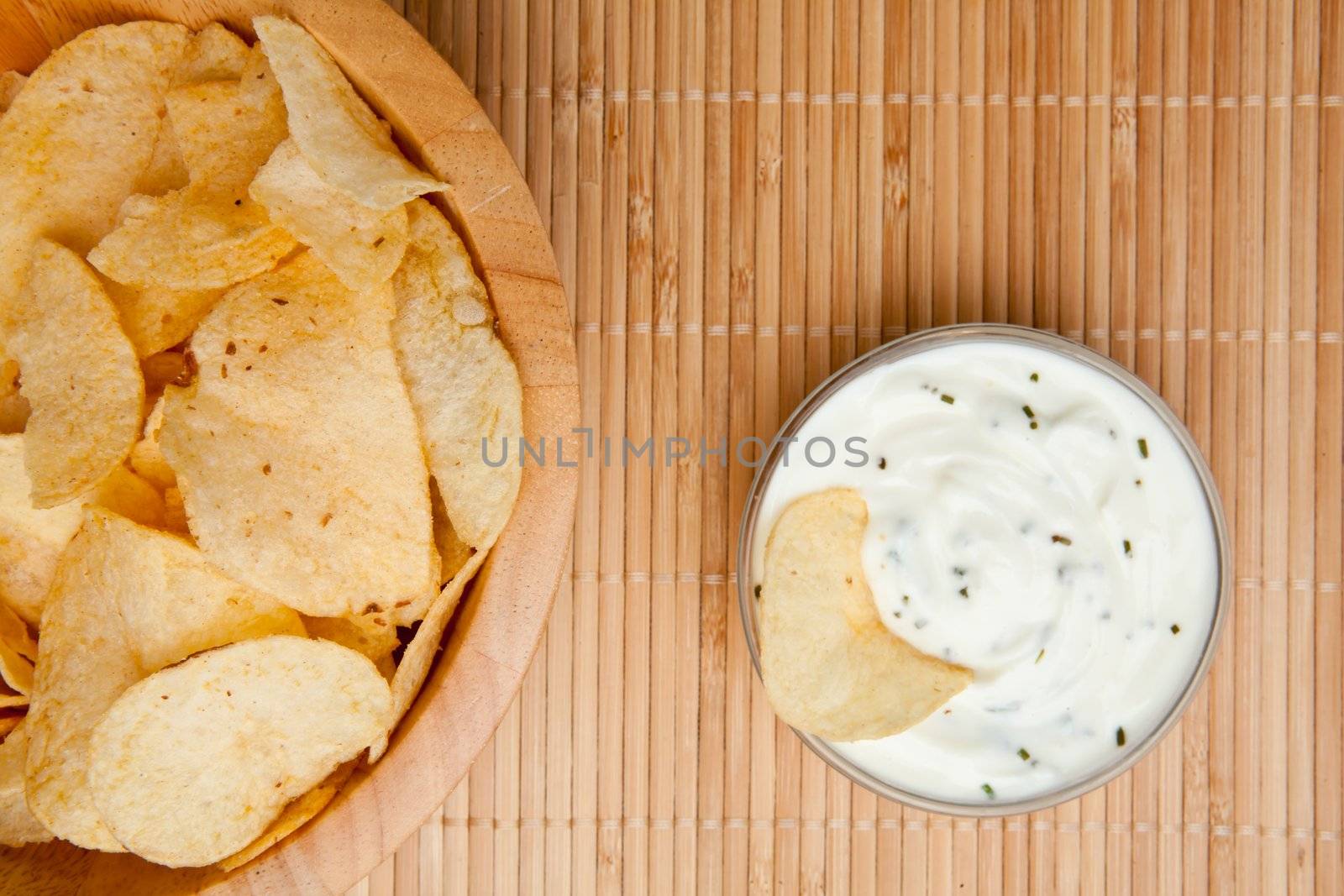 A bowl of chips and a bowl of white dip with herbs side by side