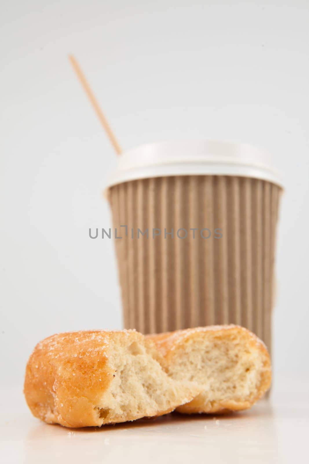 An half eaten doughnut and a cup of tea placed together against a white background