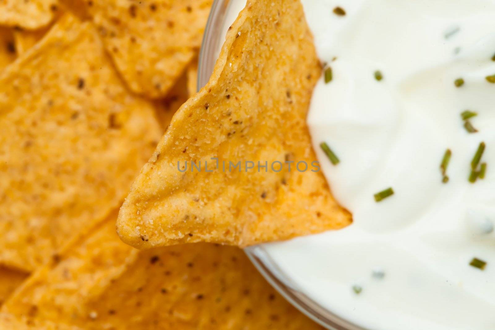 Close up of a nacho dipped into a bowl of dip with herbs