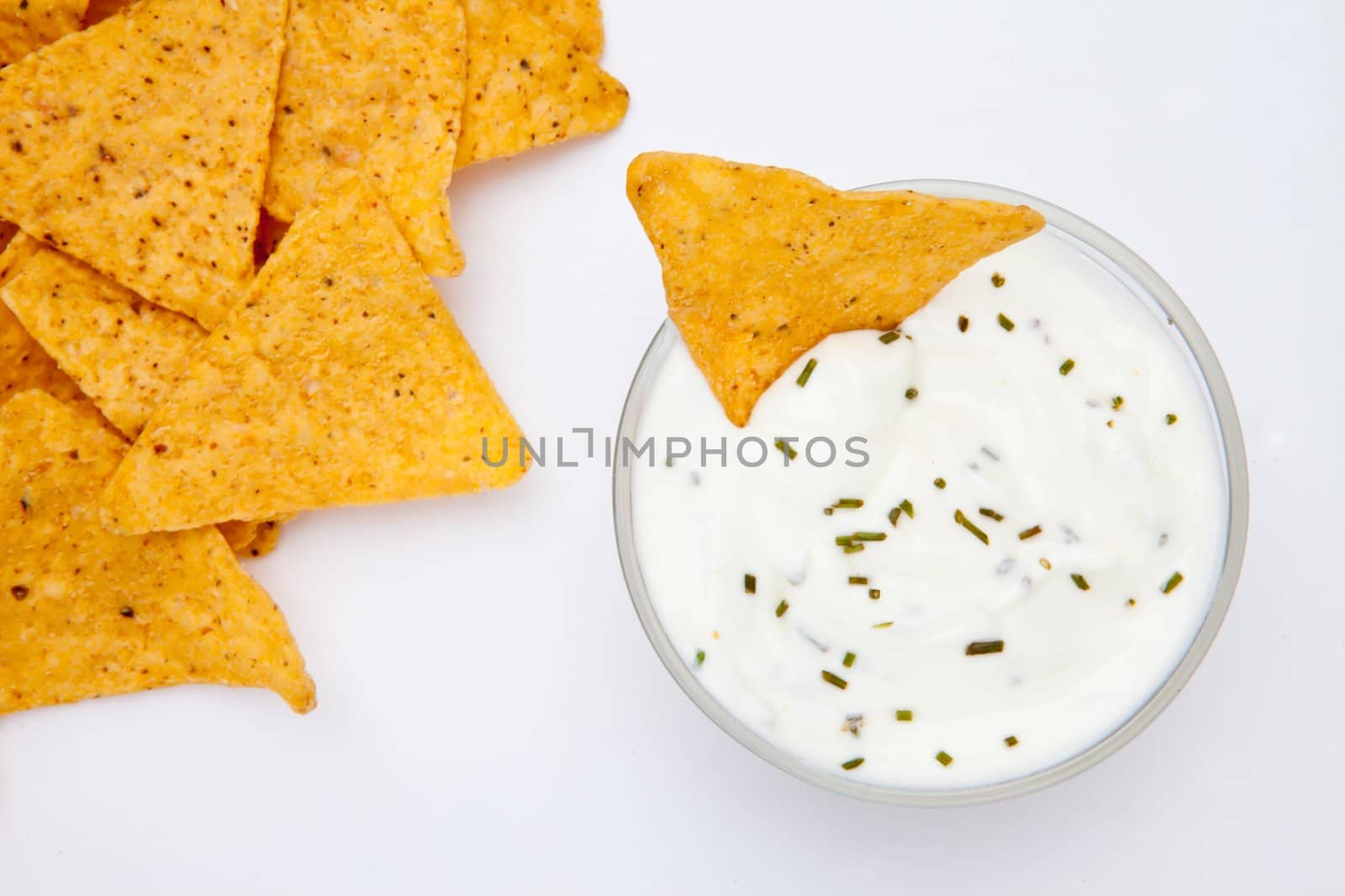 Bowl of dip with herbs with a nacho dipped in it against a white background