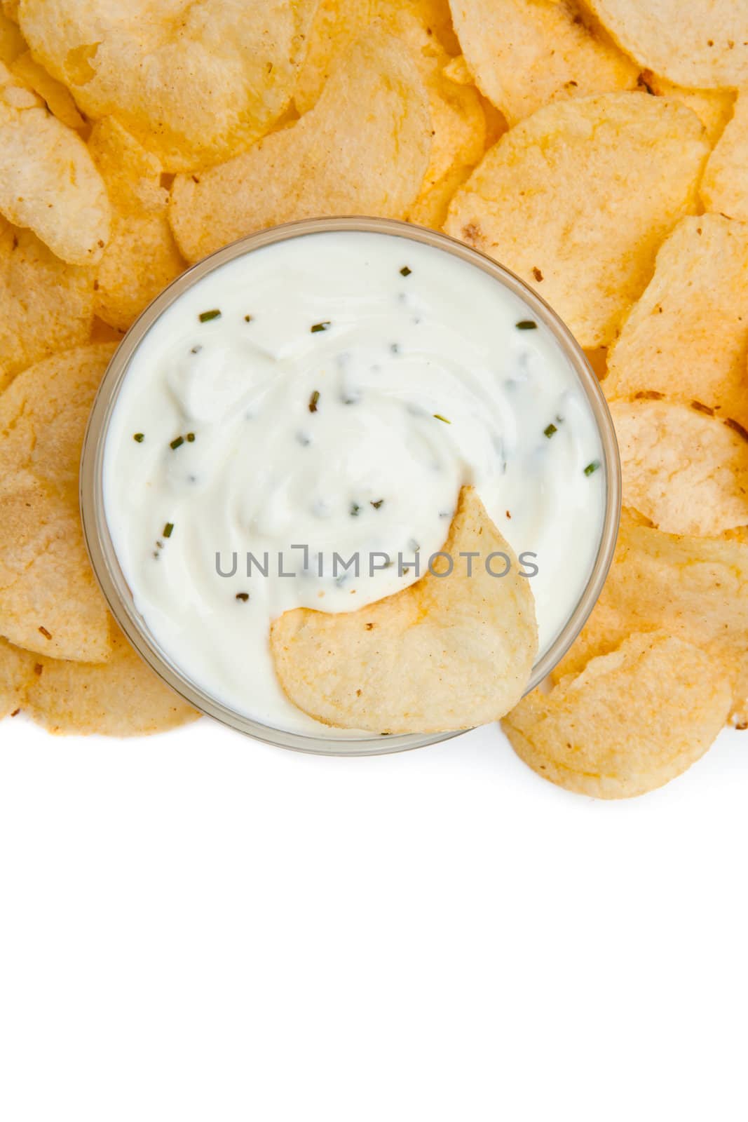 Close up of a bowl of dip with herbs ans a nacho dipped in it against a white background