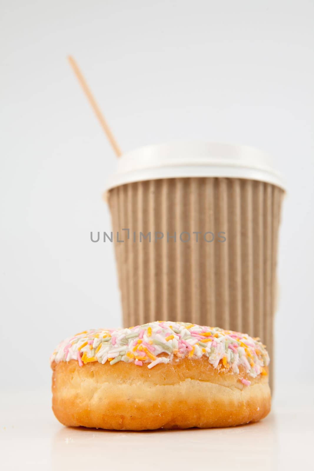 A multi coloured doughnut and a cup of tea placed together against a white background