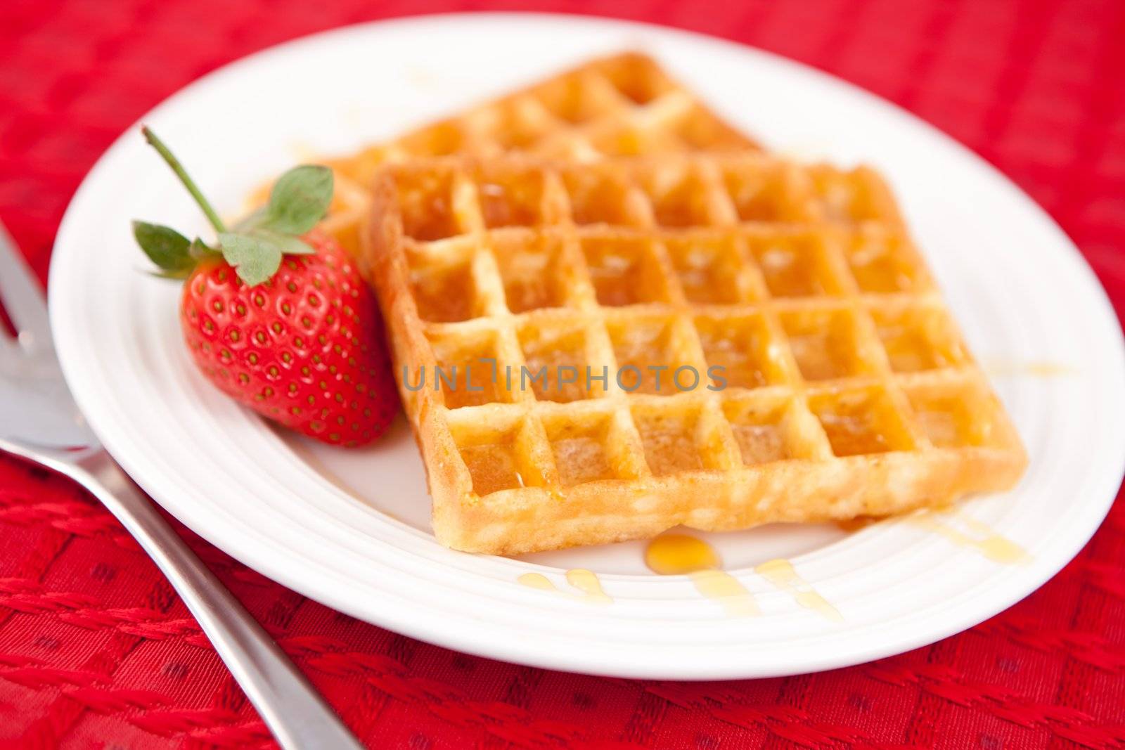 Waffles and strawberry together in a white plate om a red napkin
