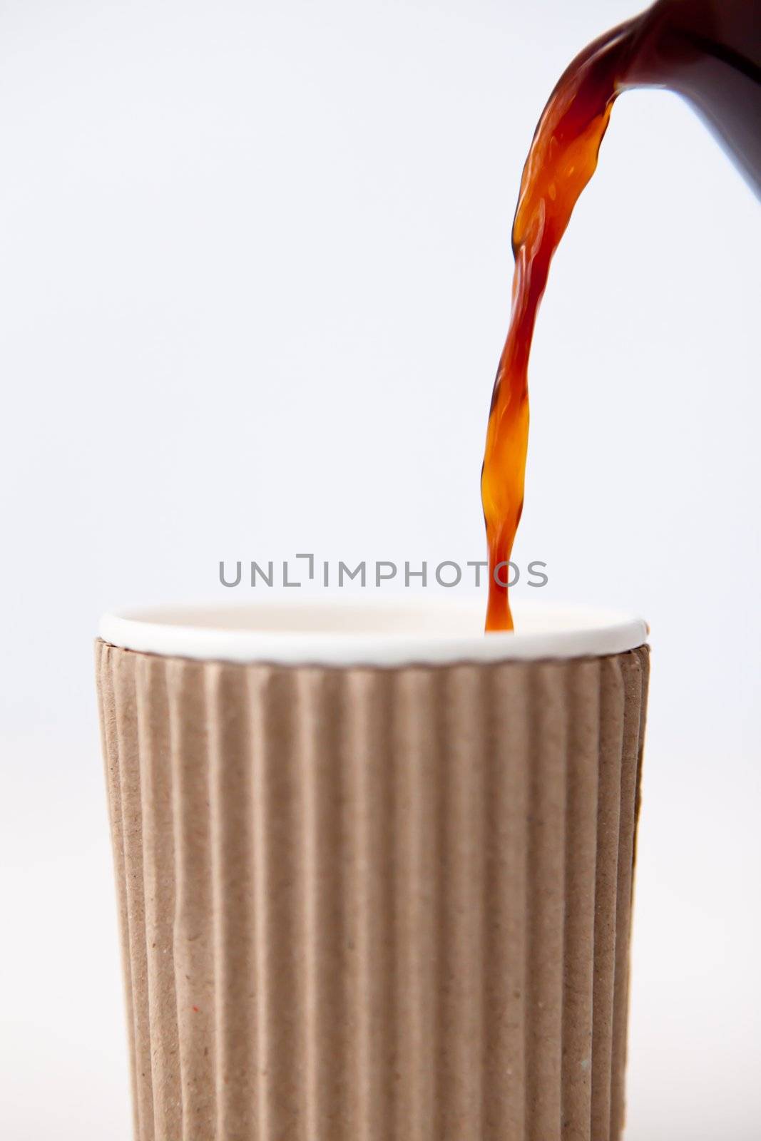 Paper cup being filled with coffee against a white background