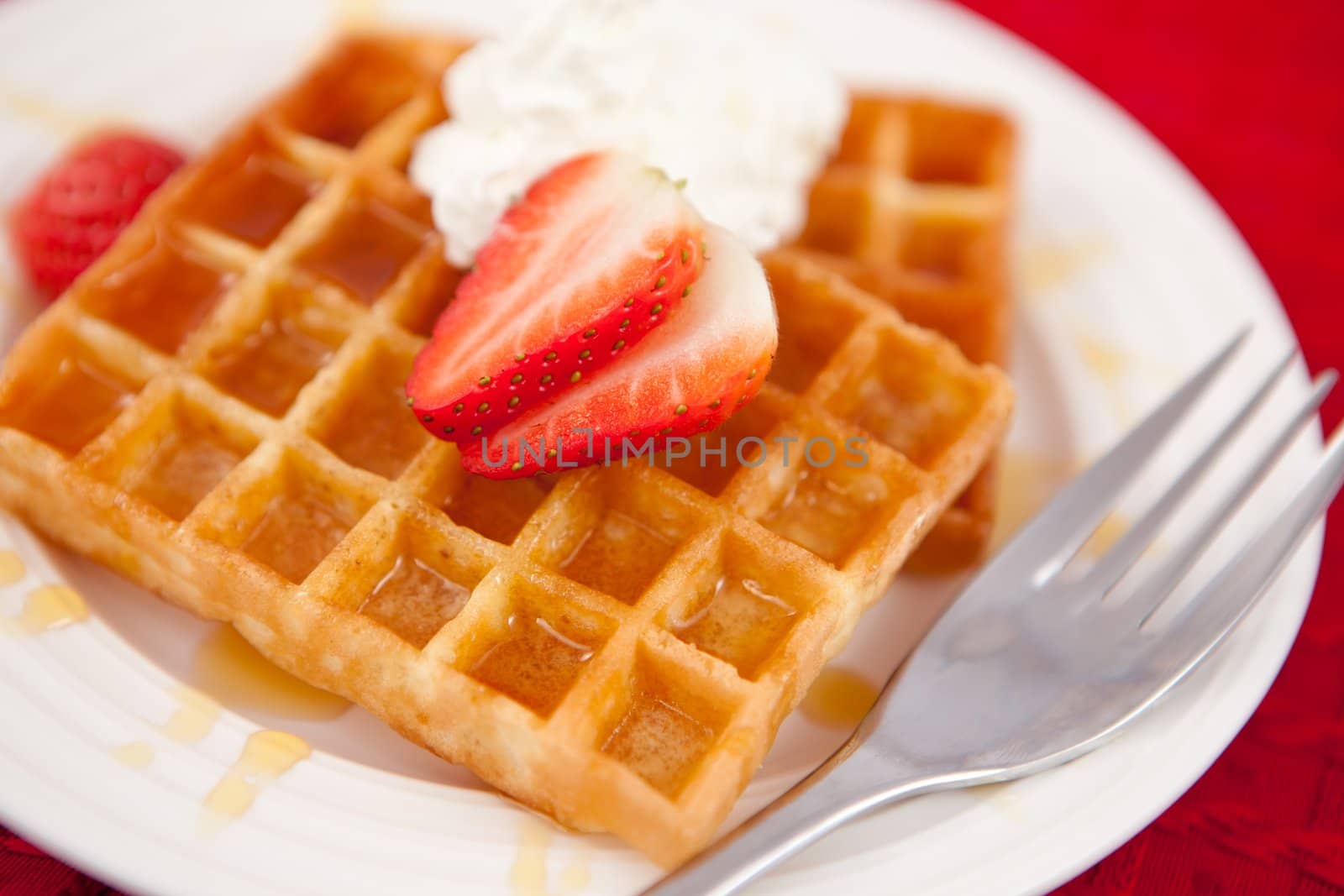 Waffles with whipped cream and strawberry on it on a red napkin