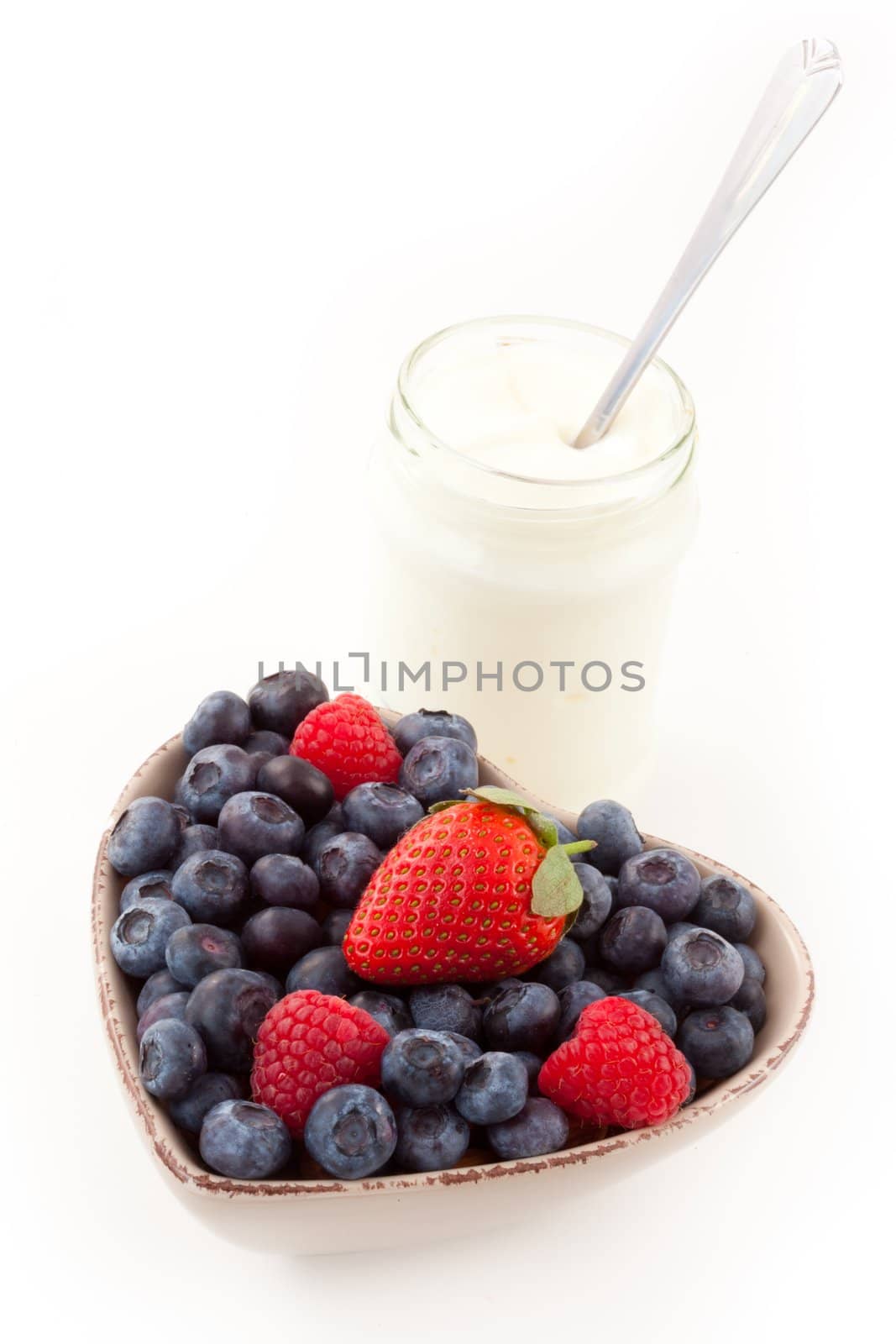 Berries in a heart shaped bowl with yogurt against a white background