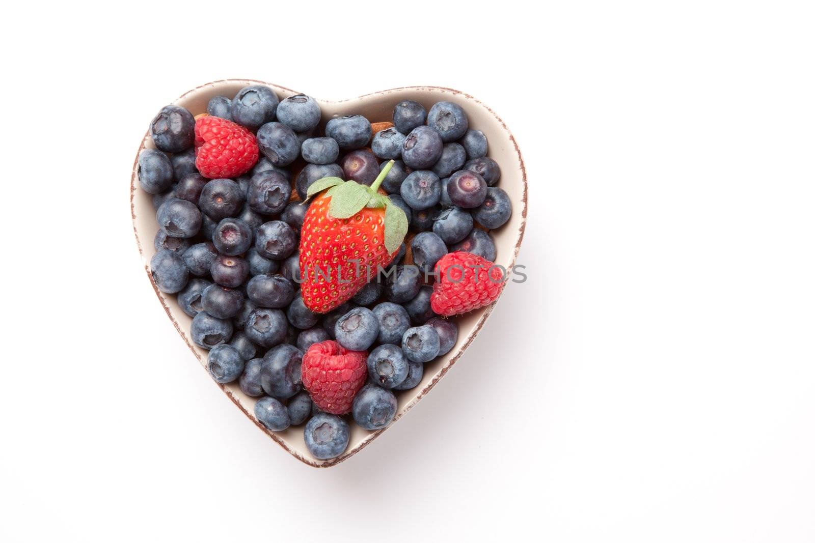 Different berries in  a heart shaped bowl against a white background