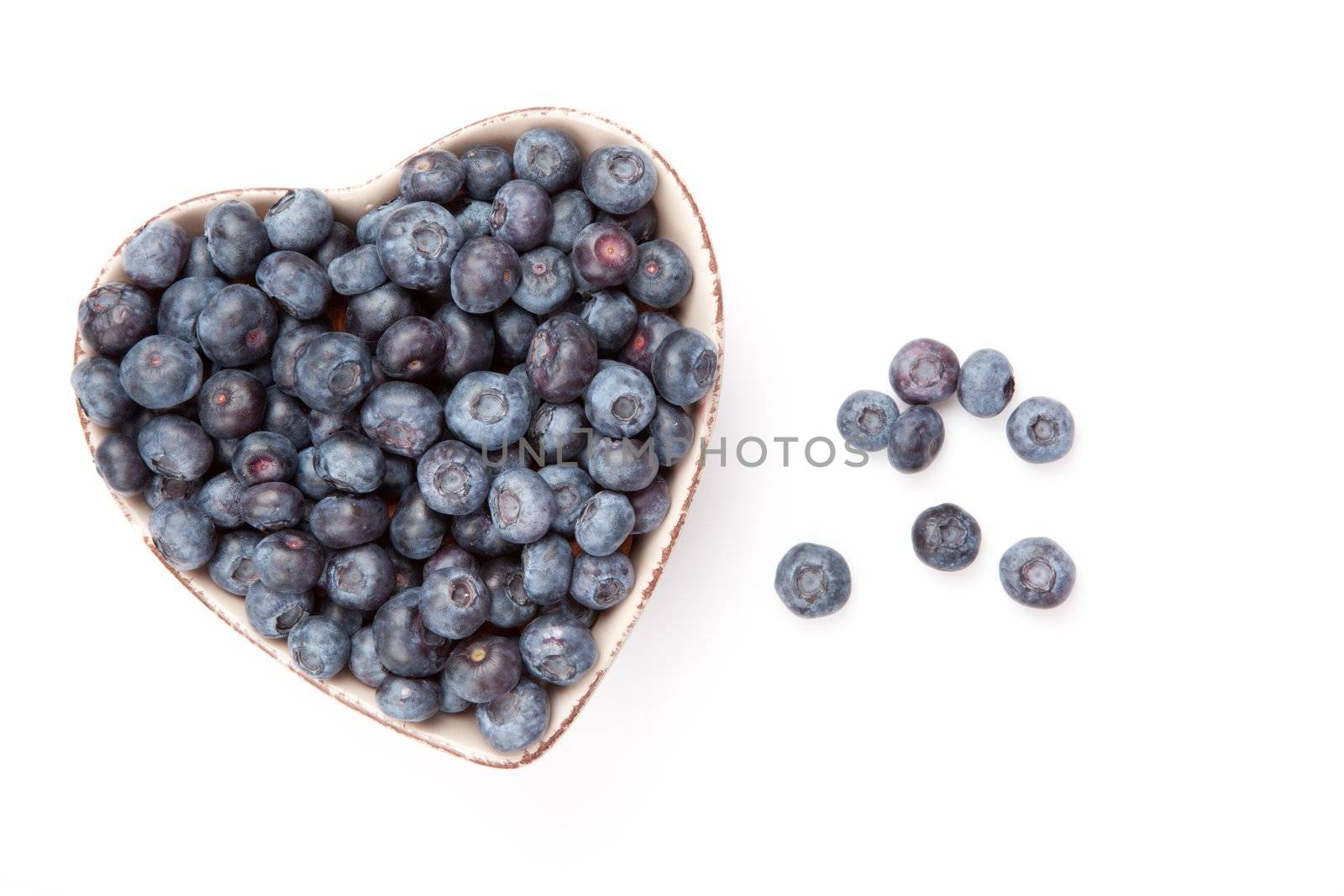 Fresh blueberries in a heart shaped bowl against a white background