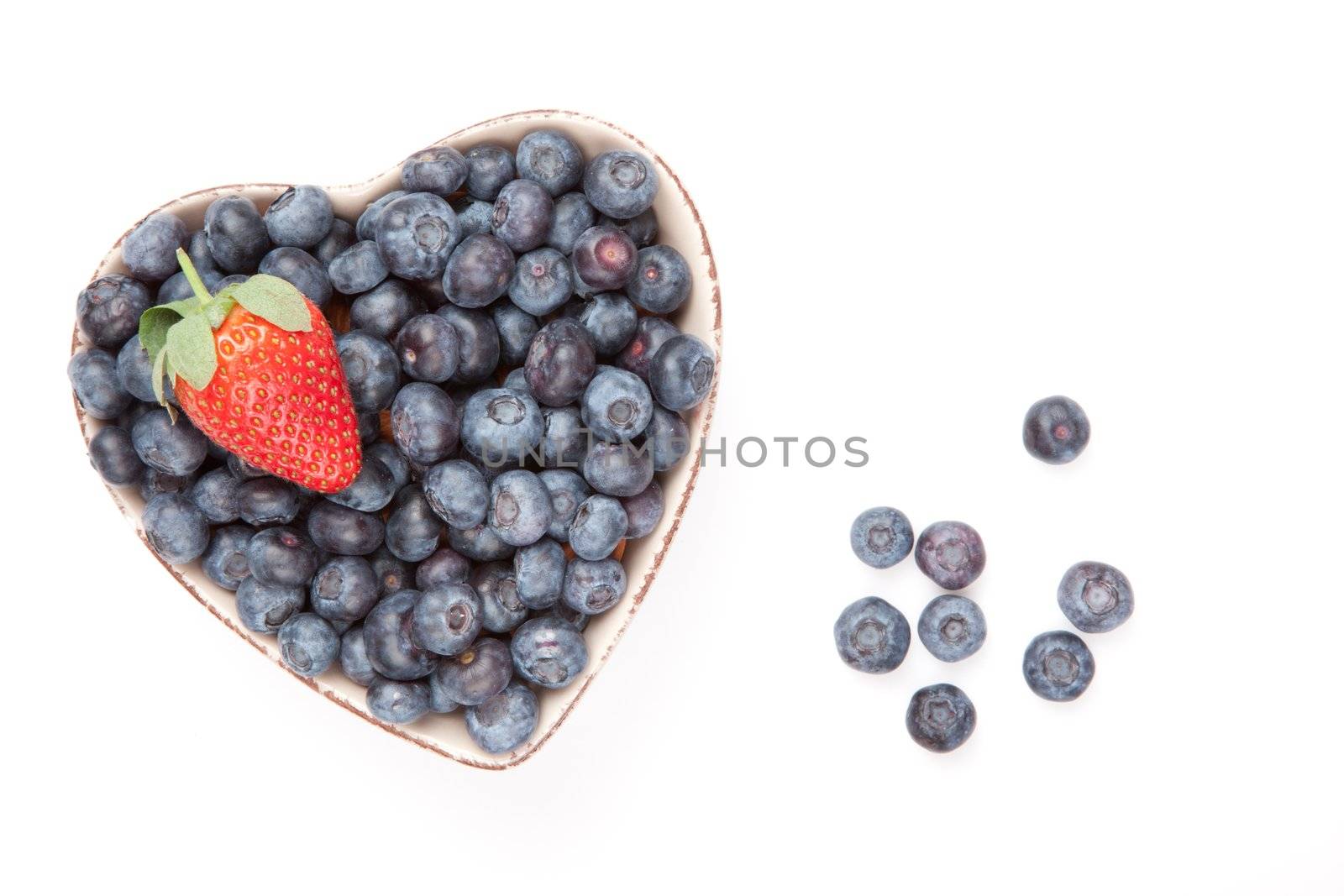One strawberry and bluberries in a heart shaped bowl against a white background