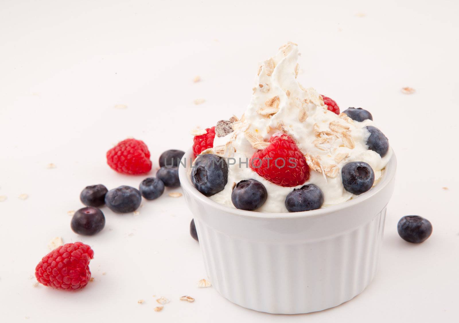 White jar of berries and whipped cream against white background