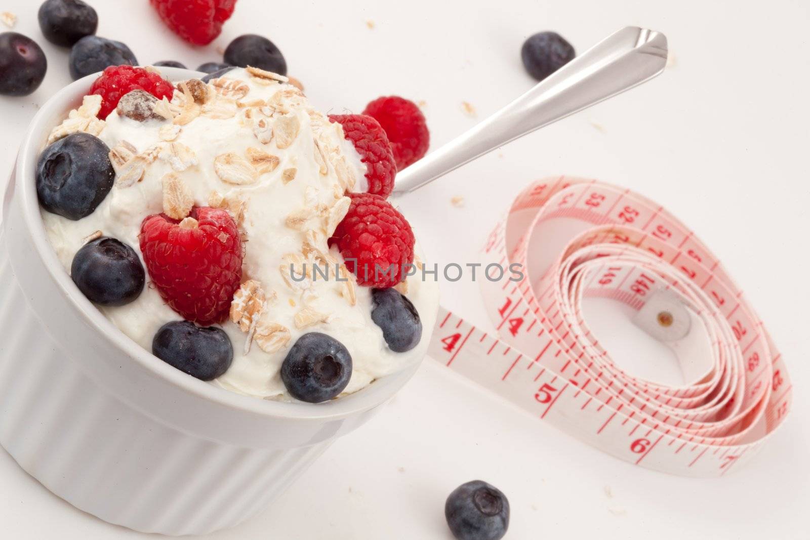 Jar of fruits and whipped cream with spoon and a tape measure against white background