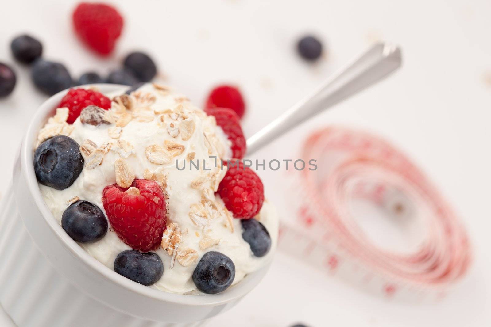 Tape measure and a jar of fruits with whipped cream against white background