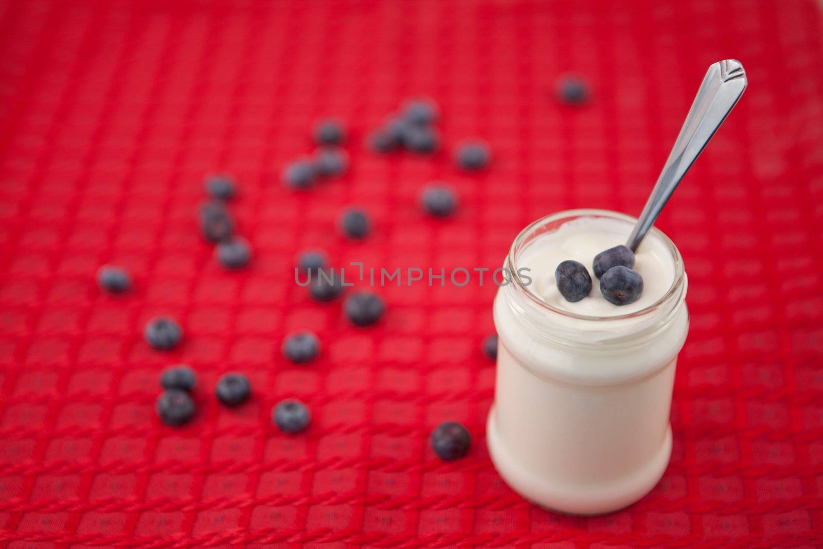 Pot of yoghurt with blueberries on a red tablecloth