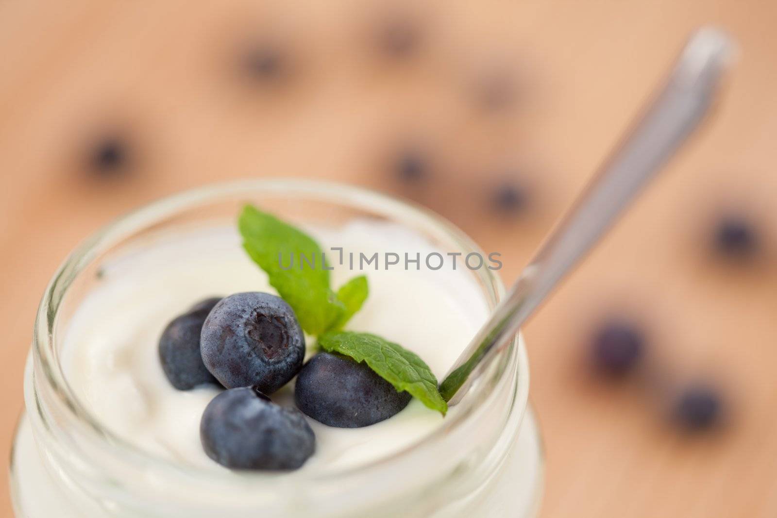 Close up of a pot of yoghurt with four leaves and blueberries by Wavebreakmedia