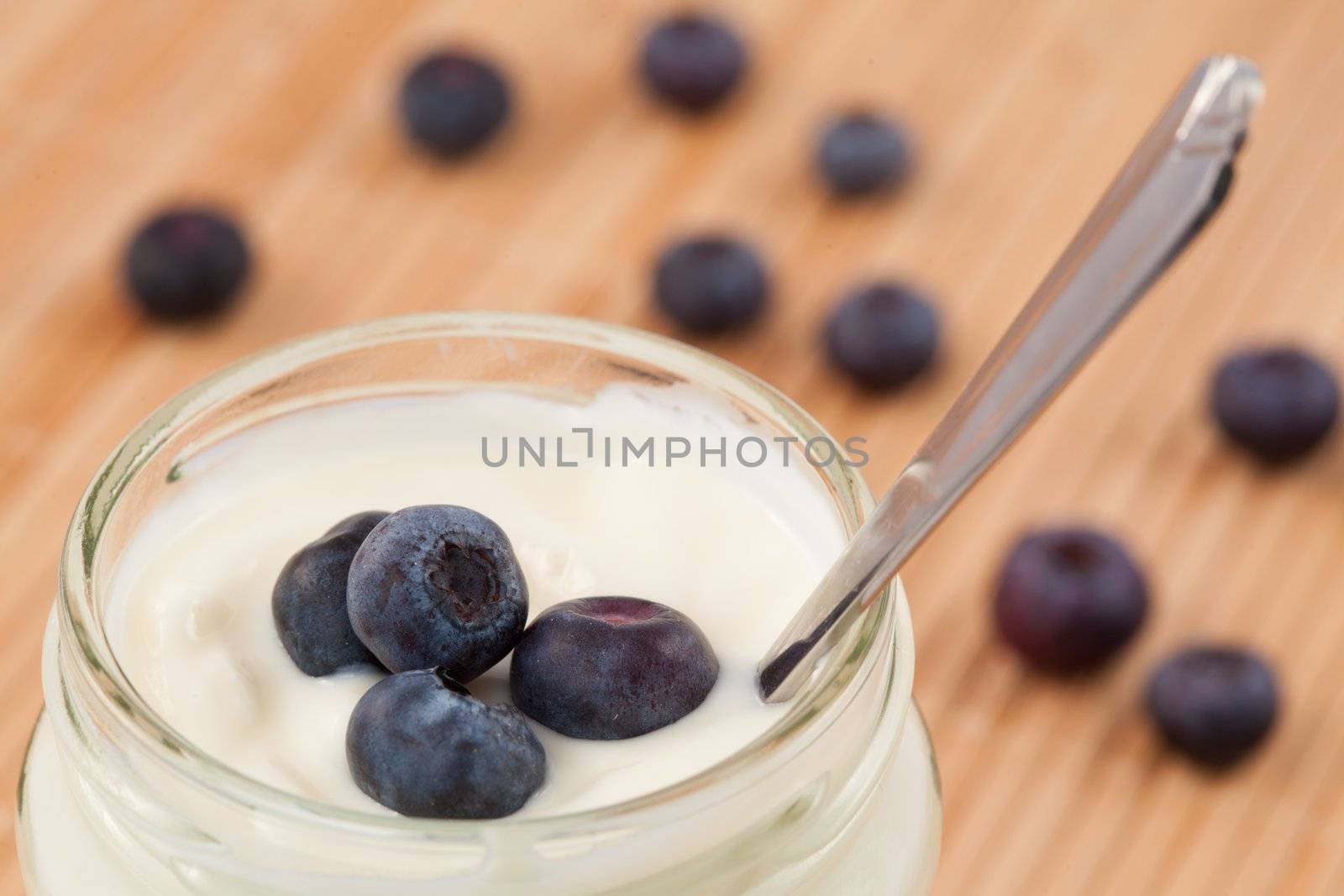 Close up of a pot of yoghurt with four blueberries displayed behind