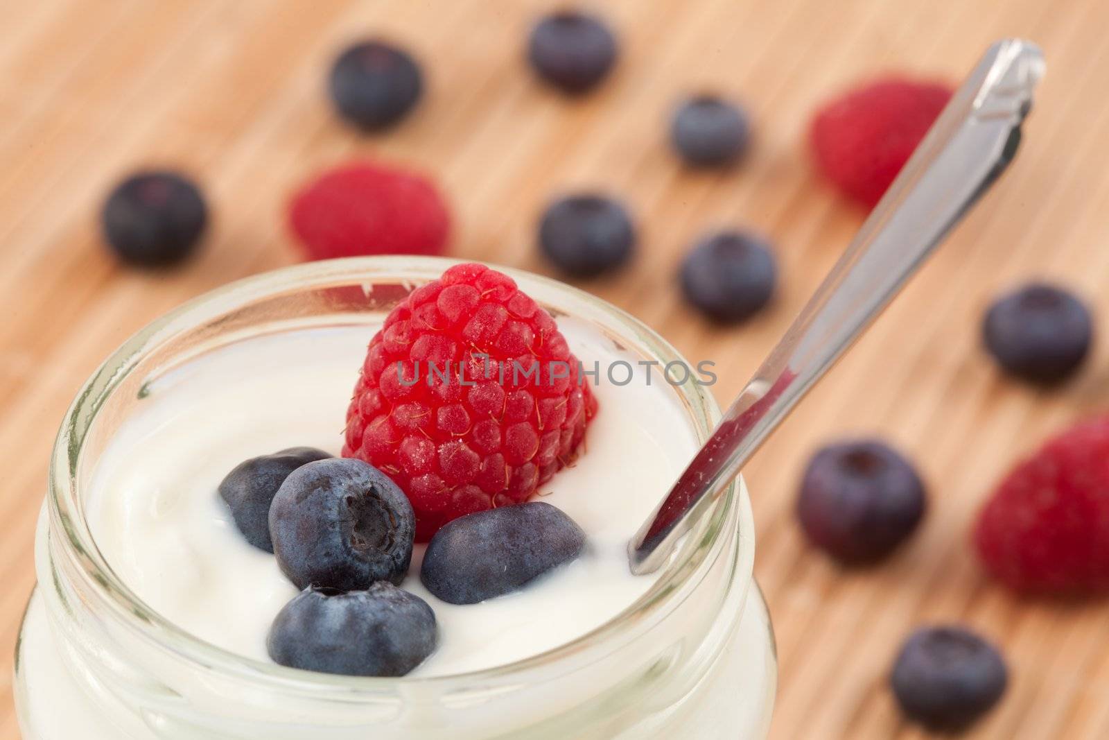 Close up of a pot yoghurt with blueberries and raspberry displayed behind