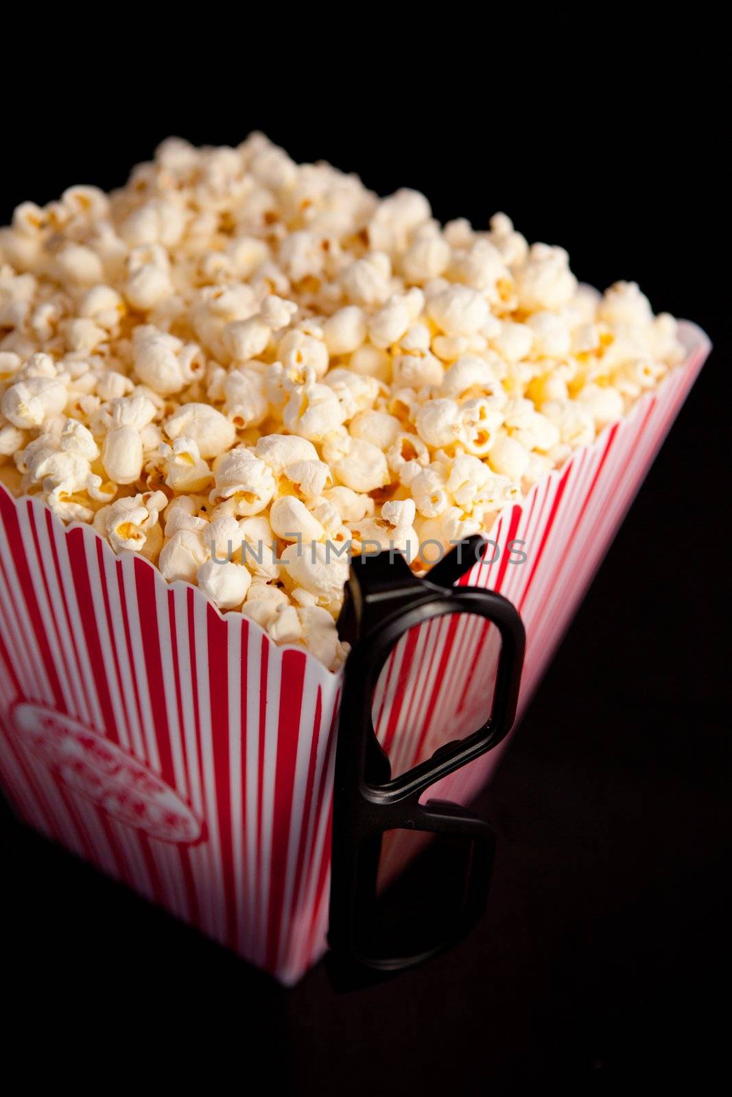 3D glasses hanging on the corner of a box of popcorn against a black background