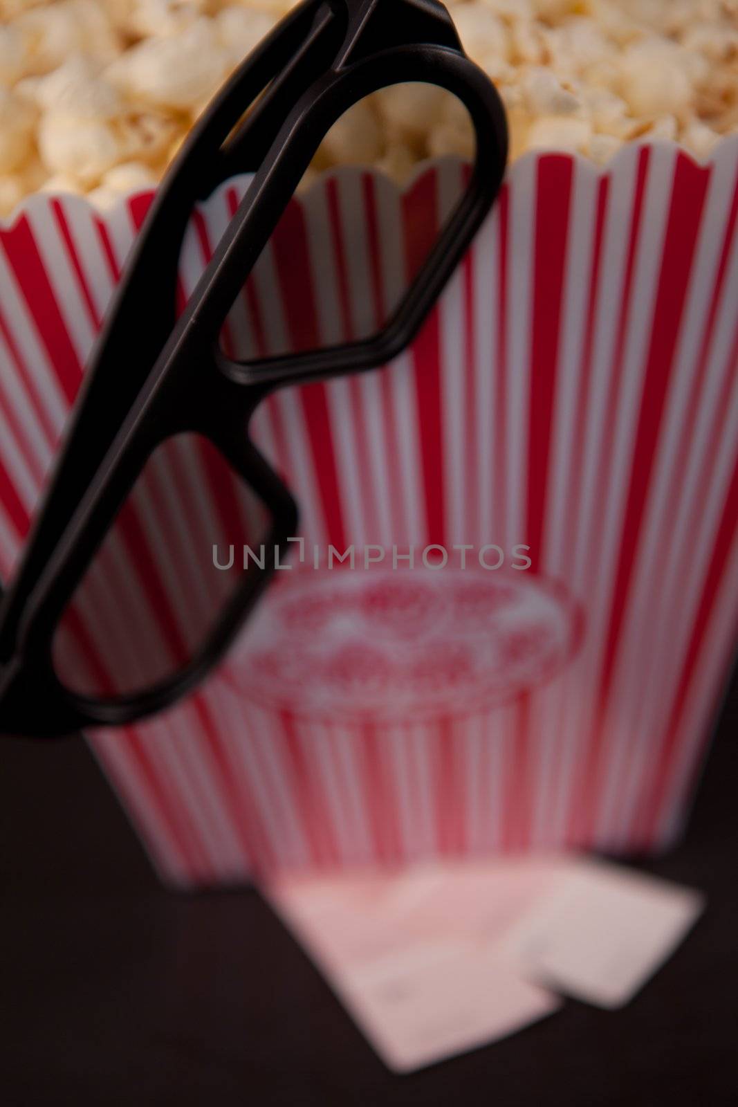 Glasses hanging on the edge of a box of pop corn standing on two tickets