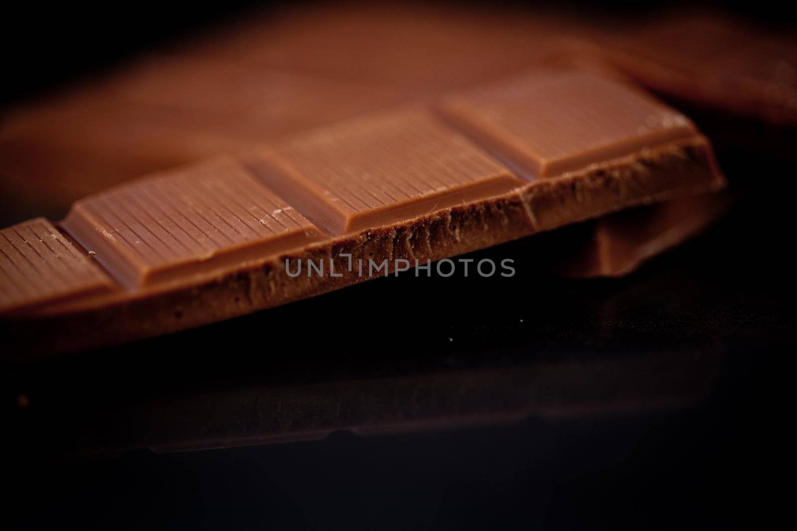Chocolate bar lying on chocolate against a black background