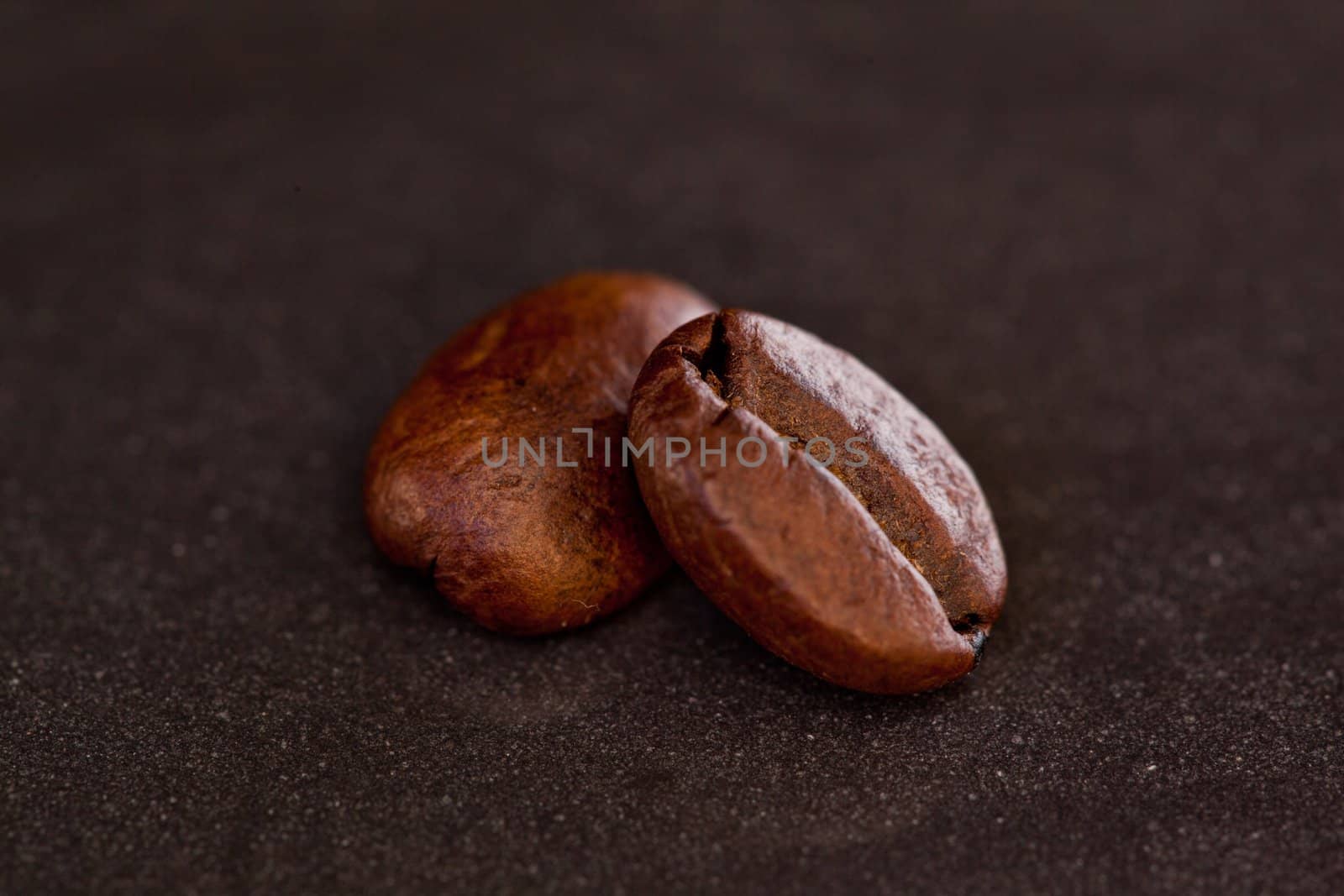 Two coffee beans on a black table side by side