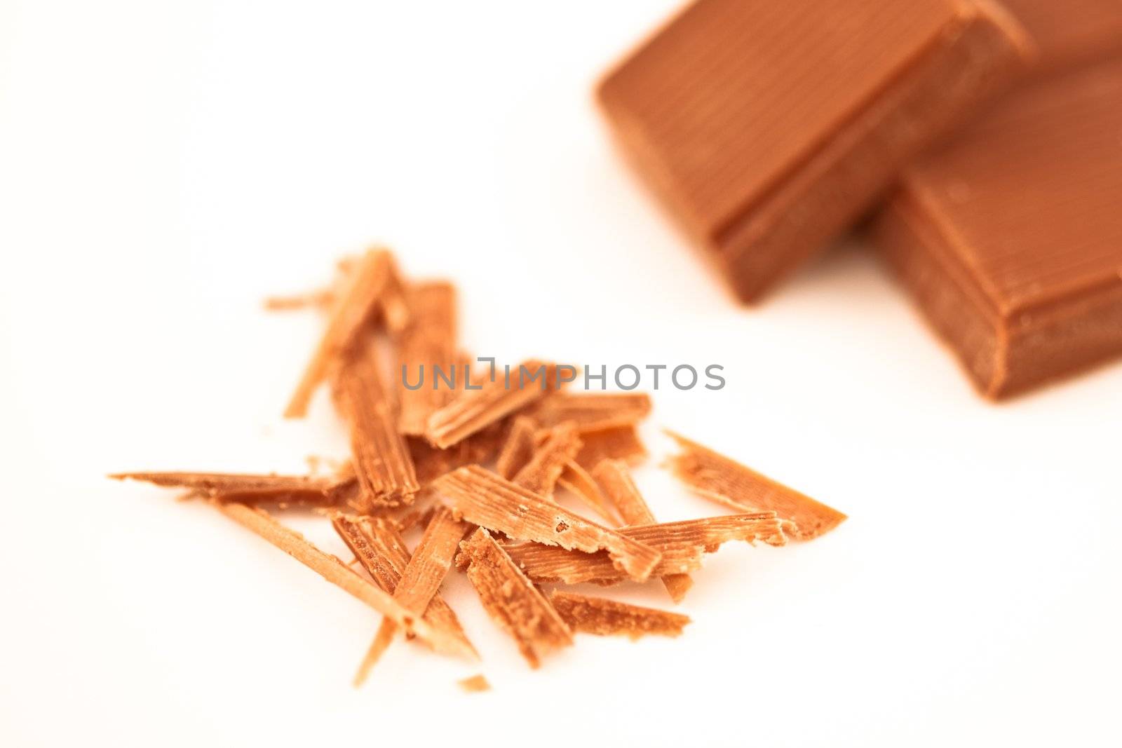 Blurred chocolate pieces and chocolate shaving against a white background