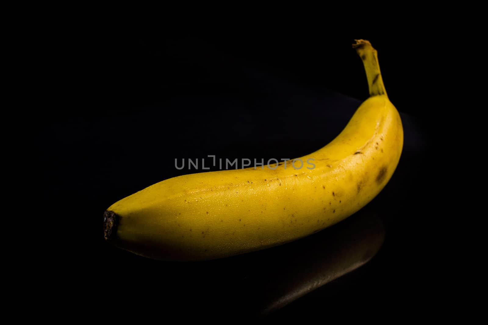 One fresh, yellow banana on black background with reflection