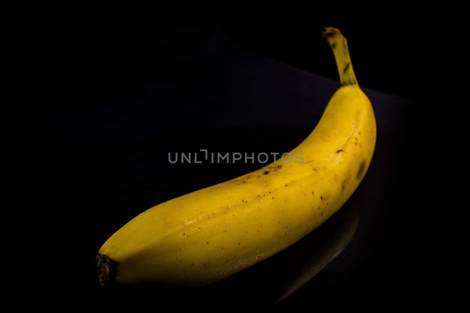 One fresh, yellow banana on black background with reflection