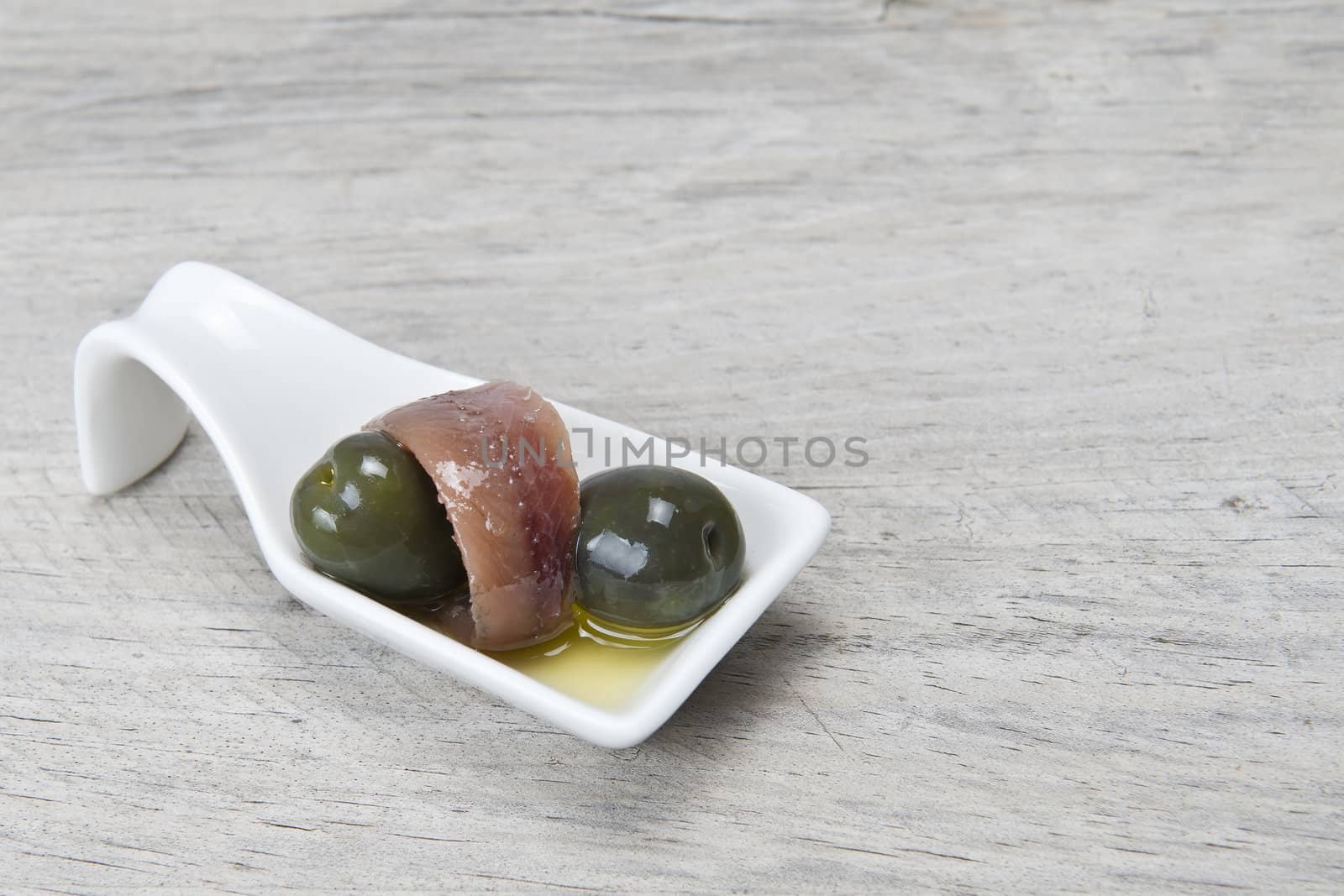 Anchovy appetizer served with green olives in a china spoon.