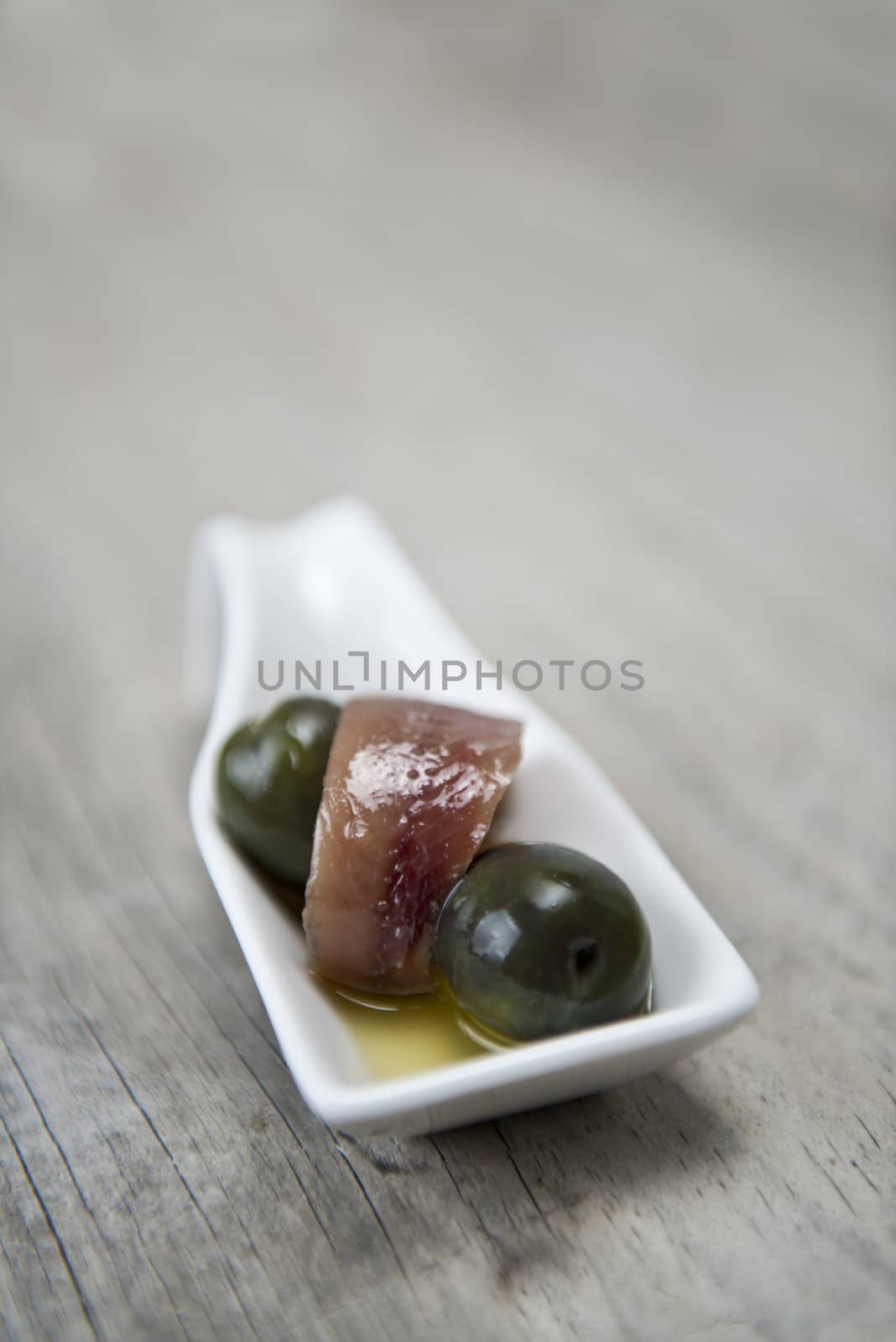 Anchovy appetizer served with green olives in a china spoon.