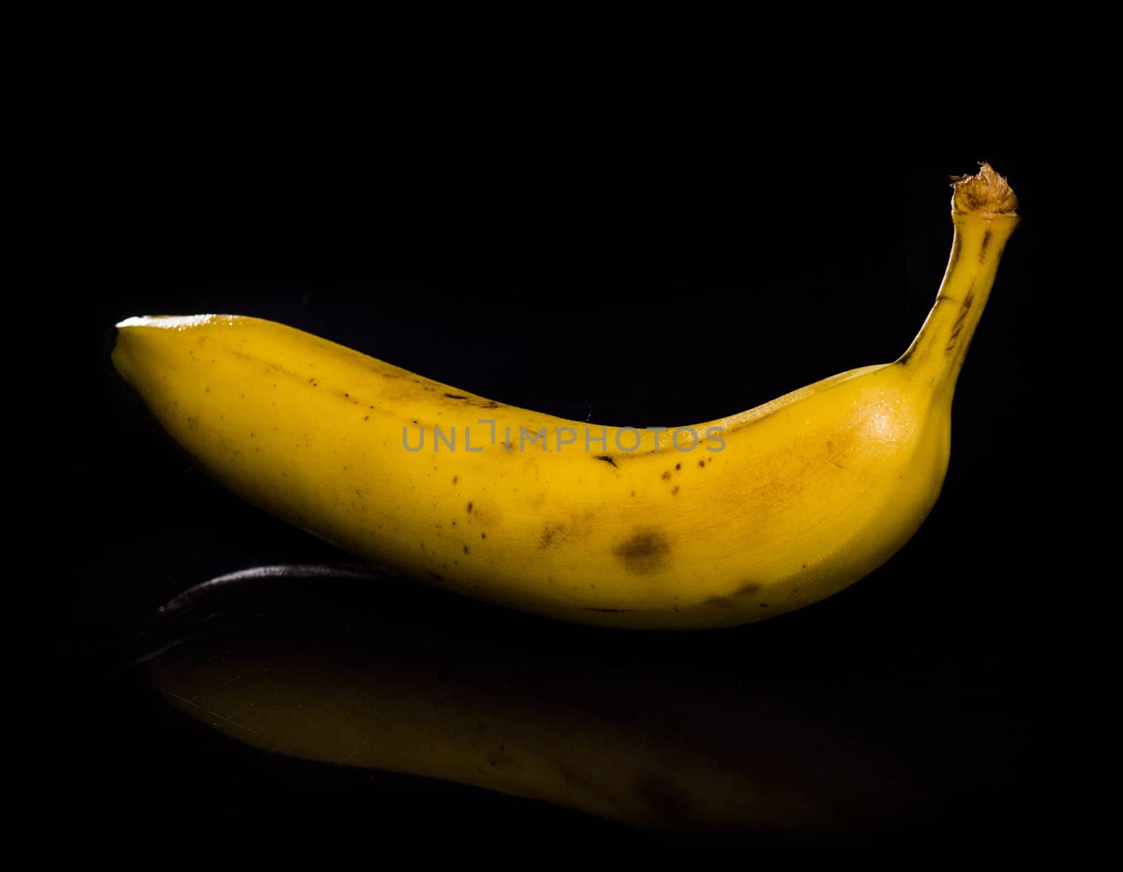 One fresh, yellow banana on black background with reflection