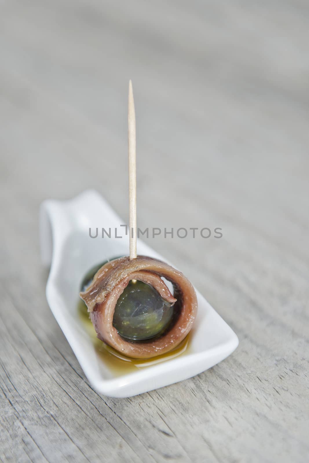 Anchovy appetizer served with green olives in a china spoon.