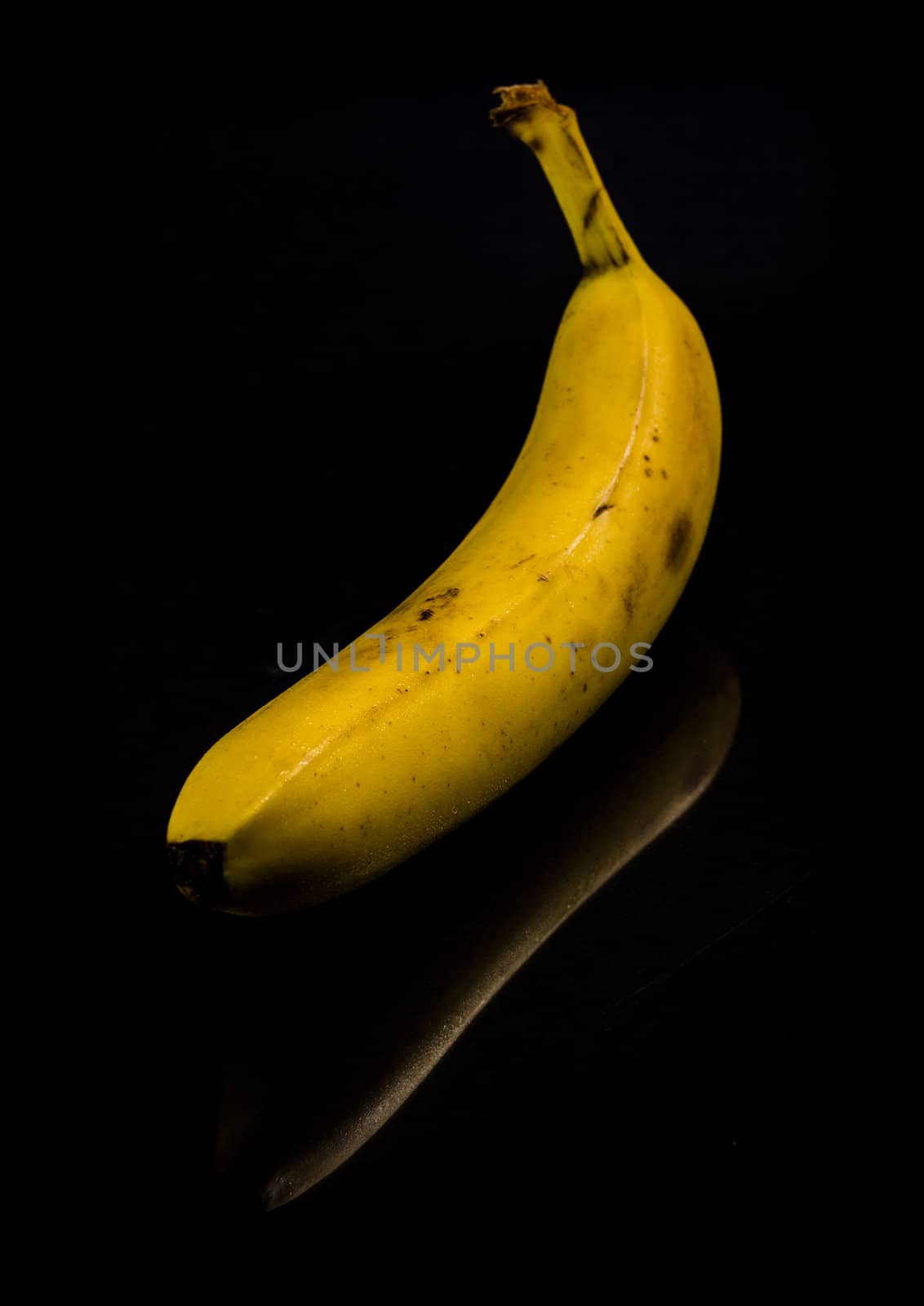 One fresh, yellow banana on black background with reflection