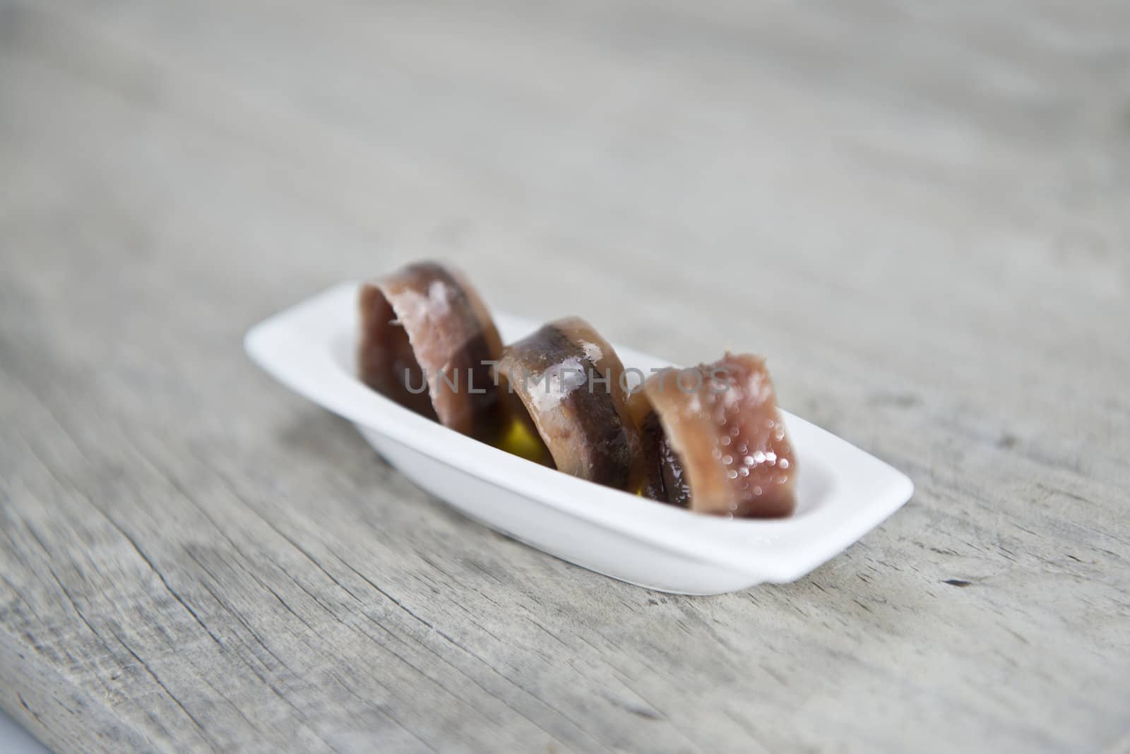 Anchovy appetizer served in a china spoon on a wooden background