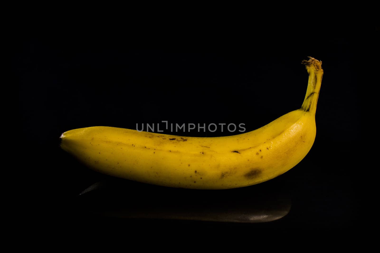One fresh, yellow banana on black background with reflection