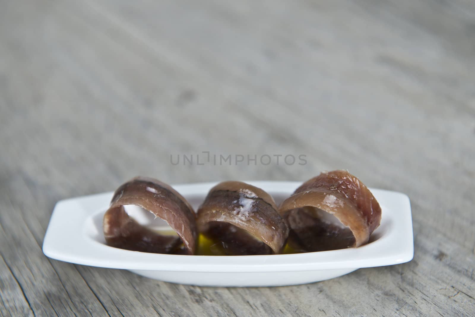 Anchovy appetizer served in a china spoon on a wooden background