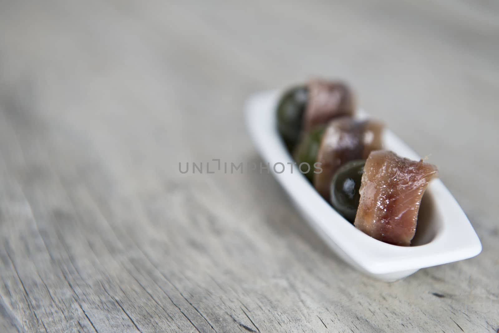 Anchovy appetizer served with green olives in a china spoon on a wooden background