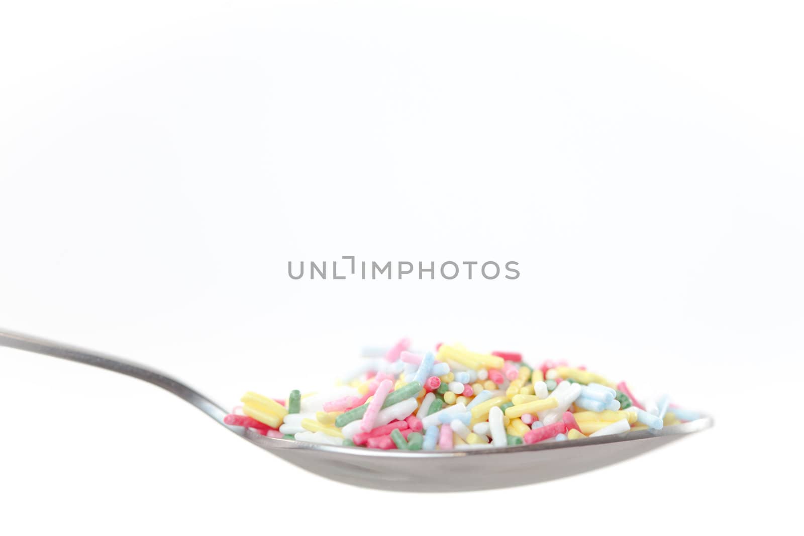 Multicolored sprinkles on the spoon on a white background