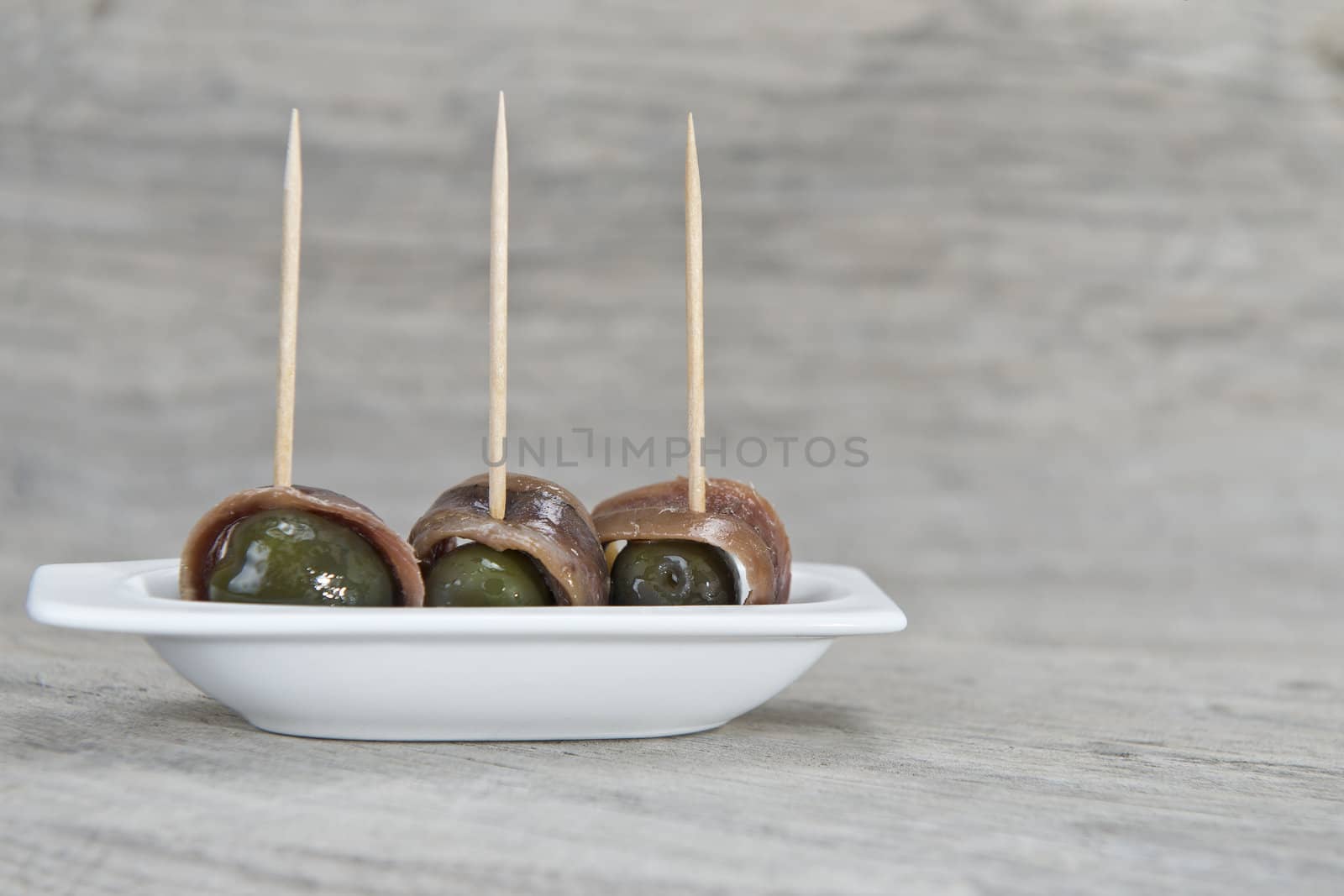 Anchovy appetizer served with green olives in a china spoon on a wooden background