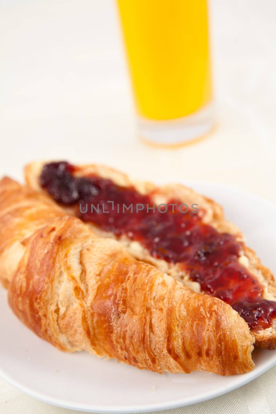 Glass of orange juice behind a croissant on a table