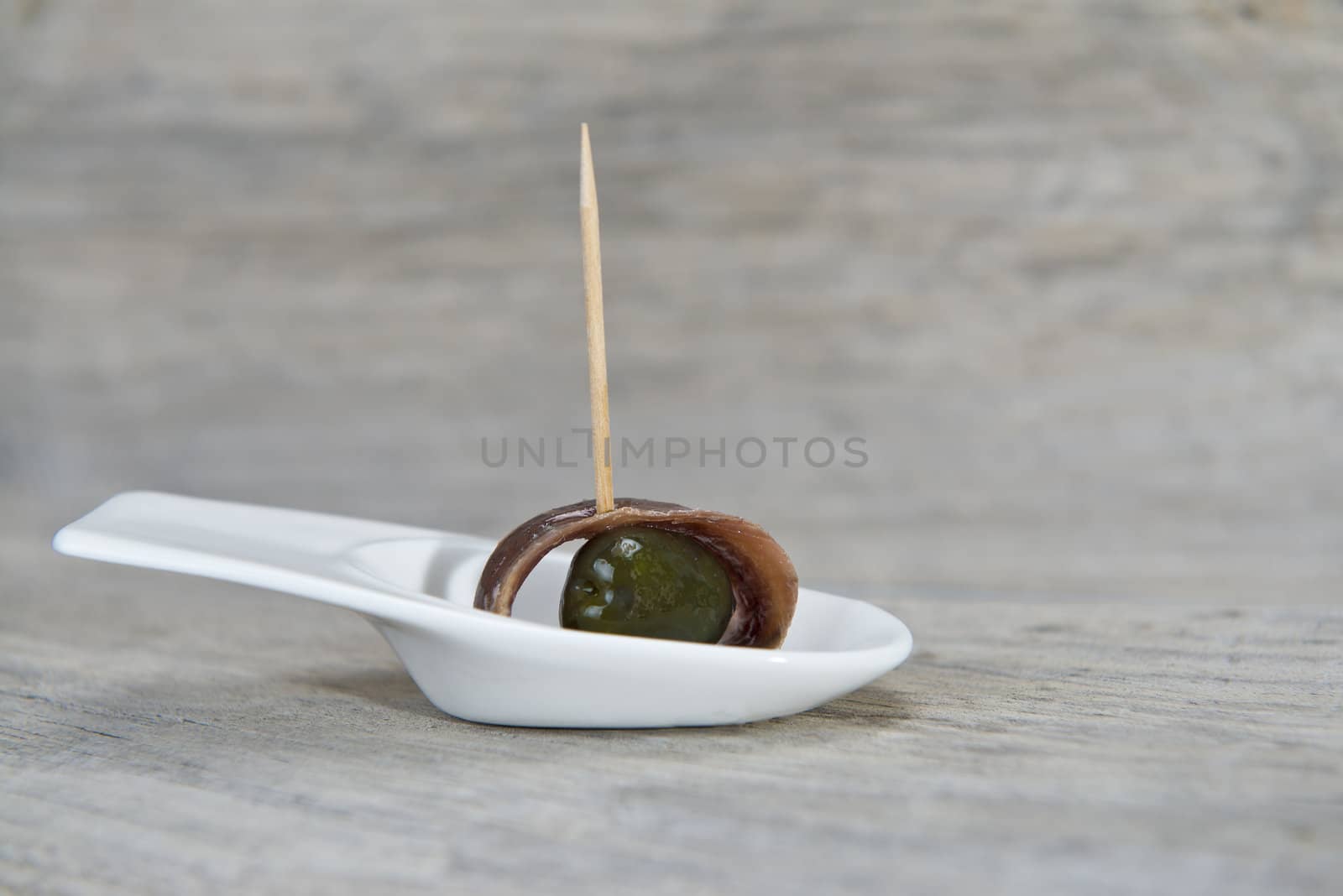 Anchovy appetizer served with green olives in a china spoon on a wooden background